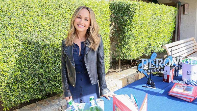 Giada De Laurentiis smiles at a table with cookbooks and Peroni promotional buckets