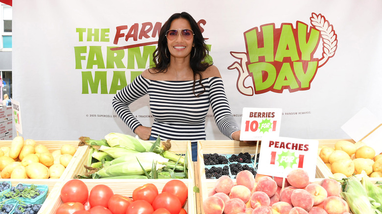 Padma Lakshmi smiles behind a produce table at a farmer's market
