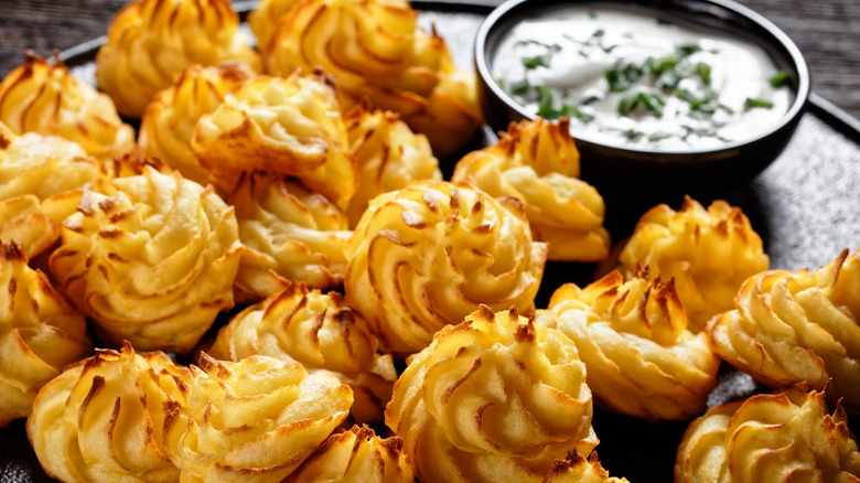 Pile of duchess potatoes on plate with bowl of dipping sauce