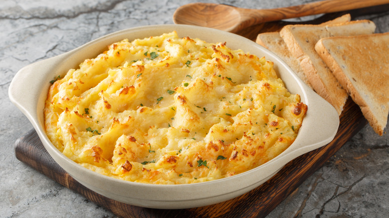 A small serving dish of potato filling, on a board with some bread slices