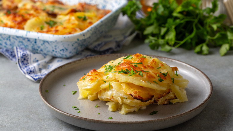 Savoy potatoes on a plate next to a baking dish and some fresh herbs