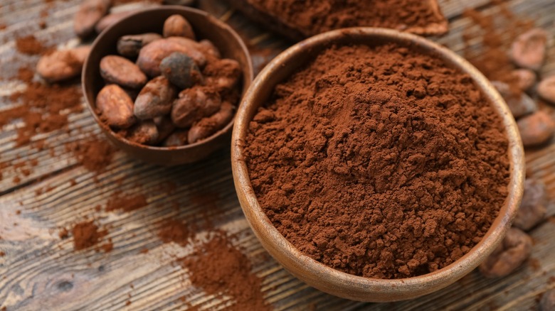 Cocoa powder and beans in two separate bowls on wooden surface