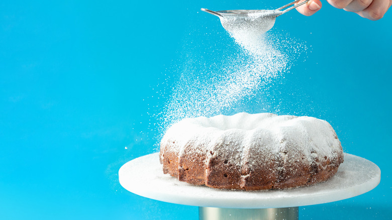 A hand sprinkles powdered sugar onto a cake