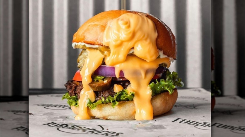 A burger from Fuddruckers topped with a lot of cheese on a table