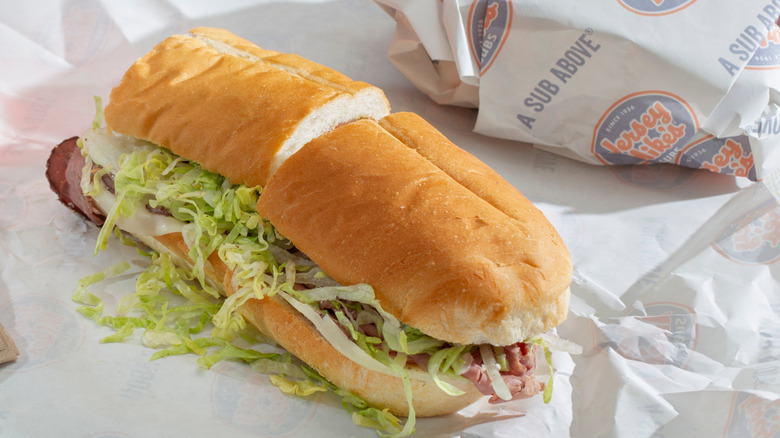 A sub from Jersey Mike's on a table with a sub rolled in paper on the side