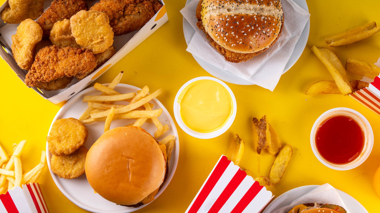 Various fast foods like burgers, fries, nuggets, and sauces on a yellow table