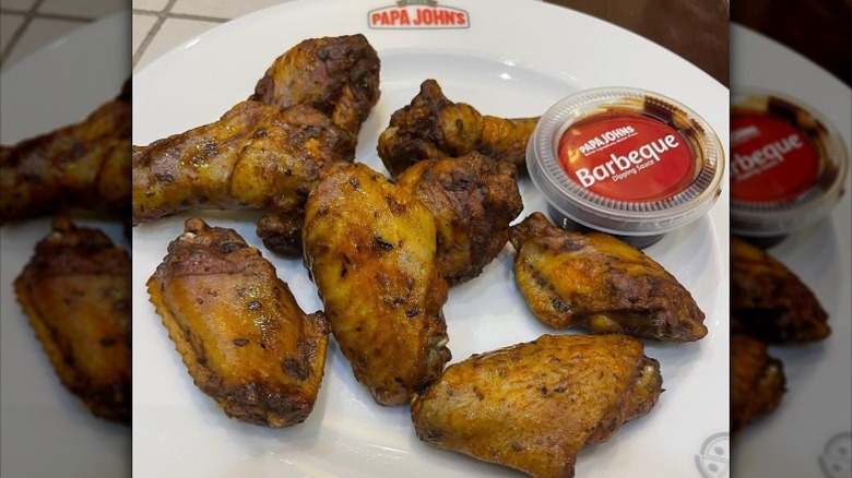 Papa John's bone-in chicken wings on a white plate with a cup of barbecue sauce