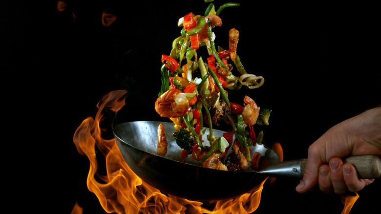Food is tossed in a hot wok, with flames underneath it