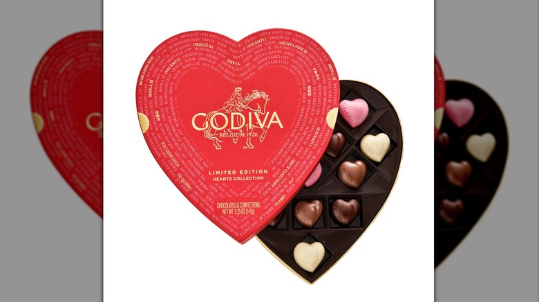 A red heart-shaped Godiva box with brown, white, and pink heart-shaped chocolates inside