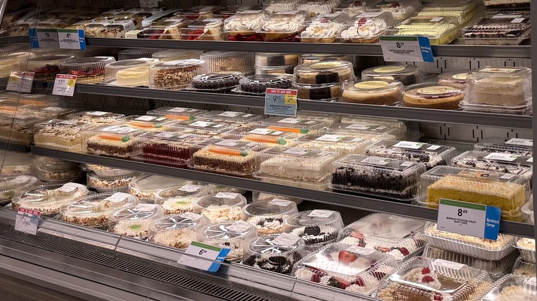 The Publix cake section, with a variety of different cakes in plastic containers on refrigerated shelves