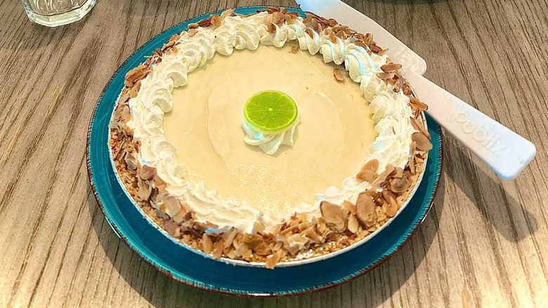 Publix key lime pie on a blue plate on a wooden table, with a Publix serving spatula resting on the side of plate