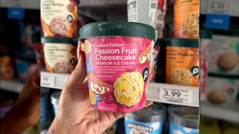 A hand holding a pint of Publix Passion Fruit Cheesecake ice cream in the store's freezer section