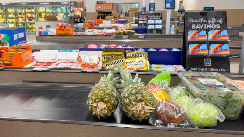 produce items for purchase on aldi cashier conveyor with candy and gift cards visible