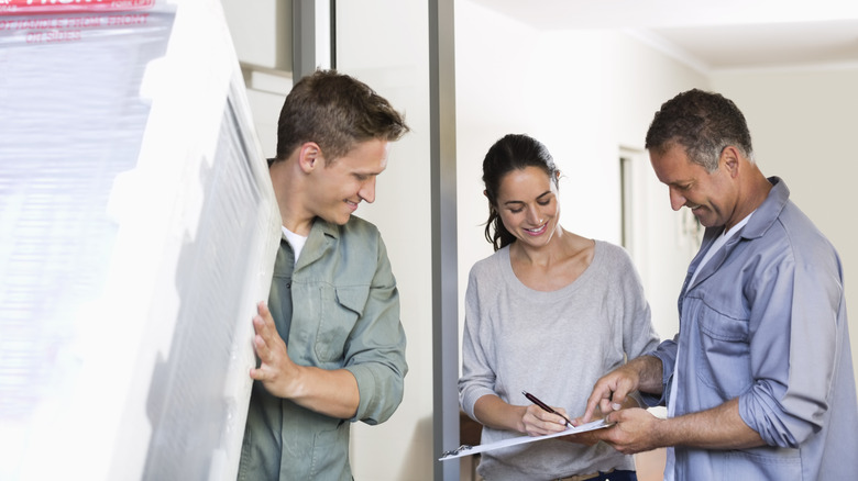 A delivery man holds a fridge while a couple sign a contract