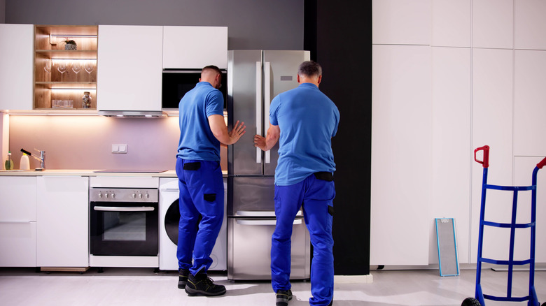 Two delivery people put a new fridge in place in a kitchen