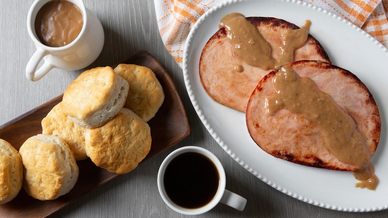 Biscuits and ham covered in gravy, with a cup of red-eye gravy