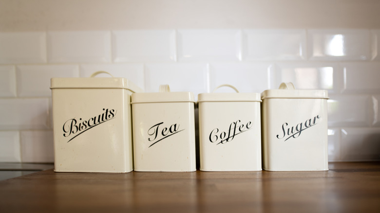 Vintage cans for tea, coffee, sugar, and biscuits, posed on a wooden kitchen countertop