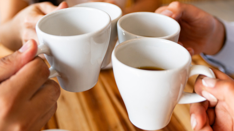 A group of people clink coffee mugs over a wooden table