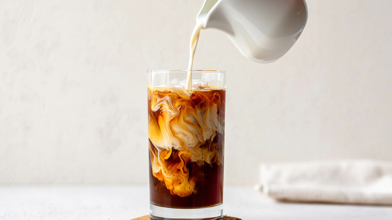 A pitcher pouring milk into a glass of coffee