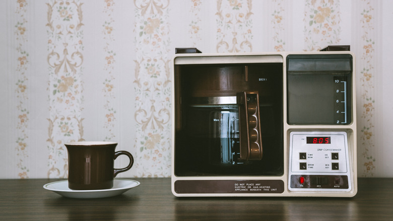 A retro coffee maker and mug posed on a wooden surface