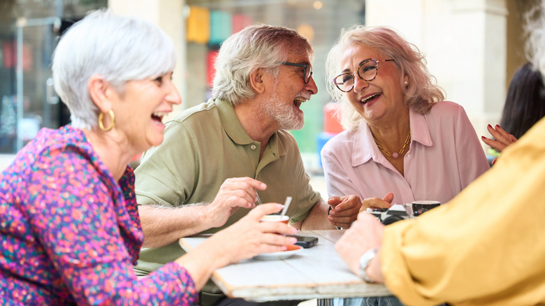 A group of older people laughing over coffee on an outdoor cafe patio