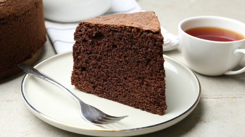 A piece of chocolate cake sits next to a cup of tea
