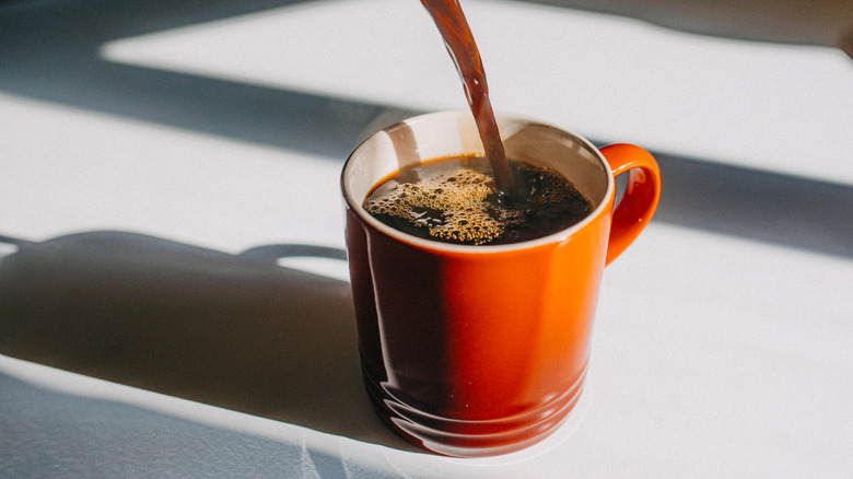 Coffee being poured into an orange mug