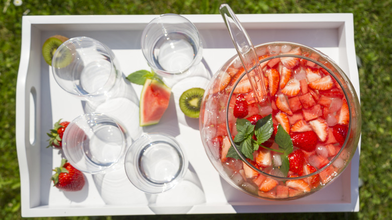 An overhead view of a fruit punch in a bowl, with glasses on a tray sitting next to it