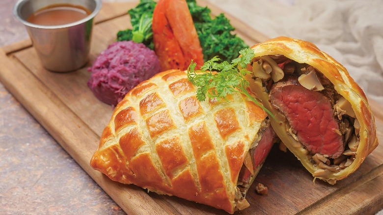 Sliced beef Wellington served on a wooden board with vegetables and garnish