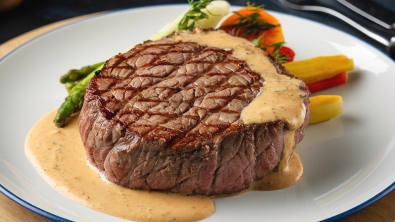 A steak served medium rare with hollandaise sauce and vegetable servings