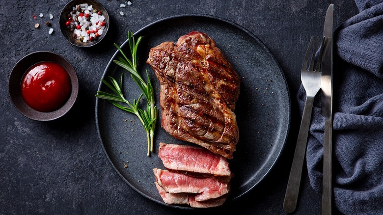 Steak cooked rare served in a grey dish with garnish and seasoning served on the side
