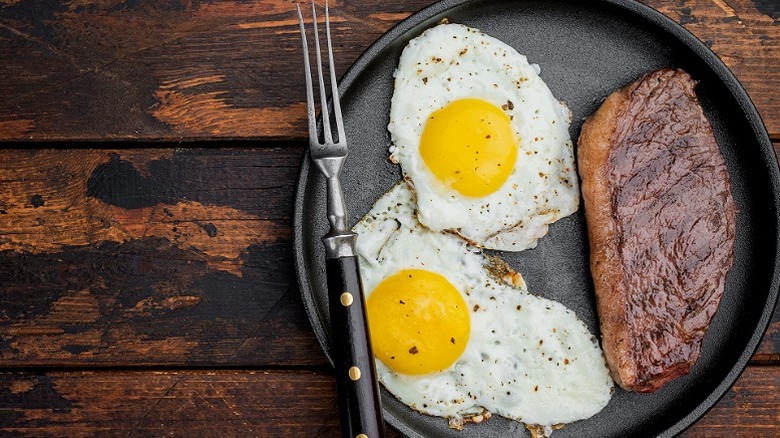 Two fried eggs and a medium steak in a grey dish on a wooden table
