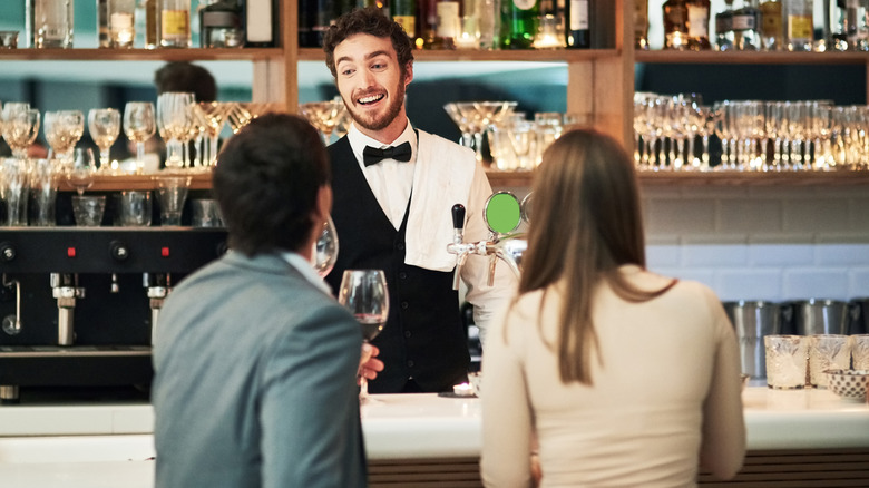 A bartender smiles as he serves two customers