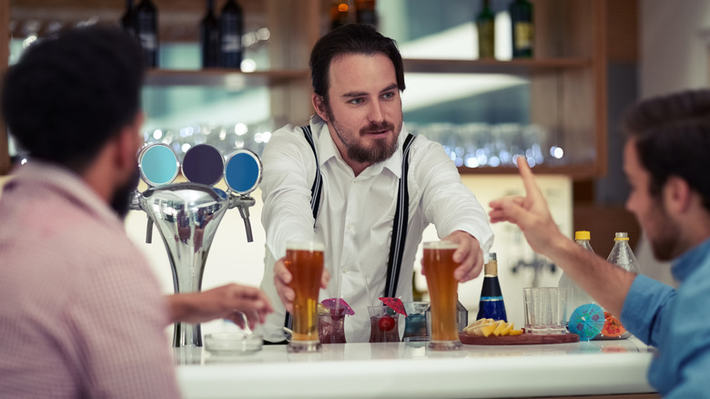 A bartender serves two beers to customers in a bar