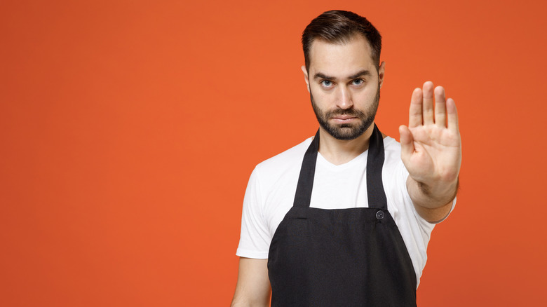 A man in an apron holds his hand up to indicate "no"
