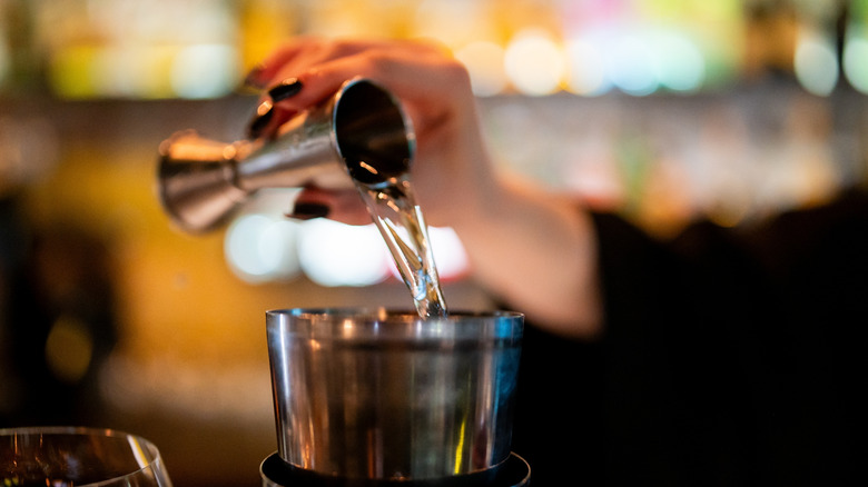 A bartender pours liquor from a jigger into a cocktail glass