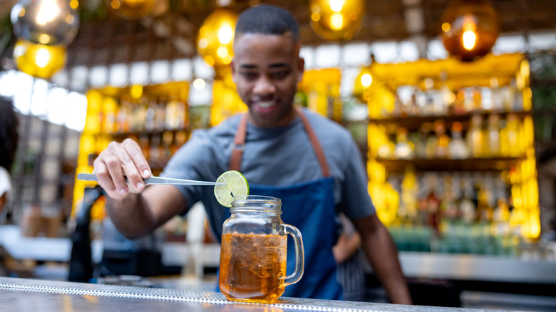 A bartender puts a slice of lime on a cocktail with a pair of tongs