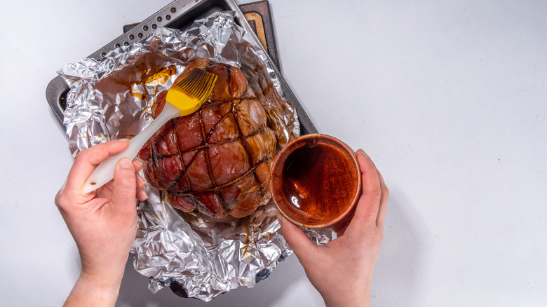 A person glazes an oven-baked ham