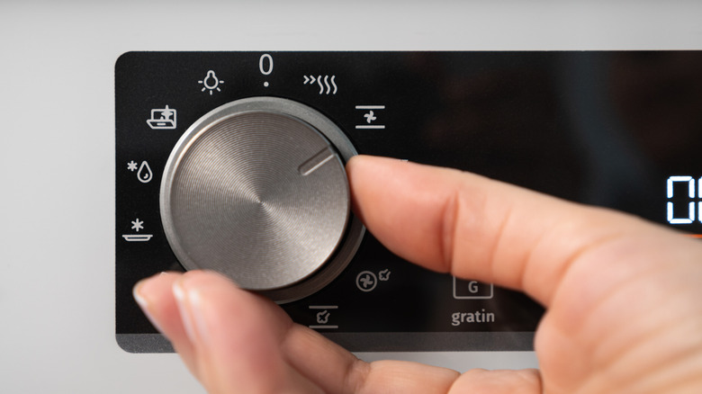 A hand adjusts an oven dial