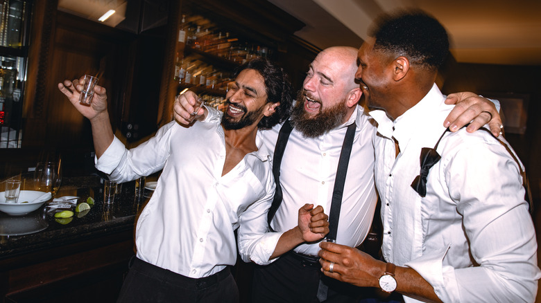 A group of drunk friends laugh while holding shot glasses