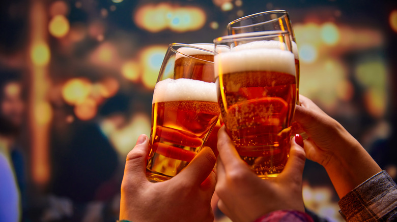 A group of hands clink glasses of beer
