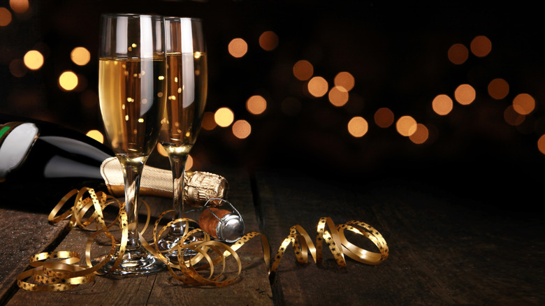 A pair of champagne glasses sit next to a bottle and a golden ribbon