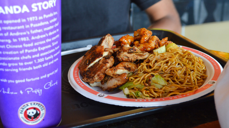 A plate of Panda Express food with a drink sitting next to it