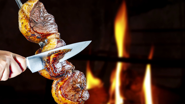 A hand slices a piece of meat from a cut of picanha