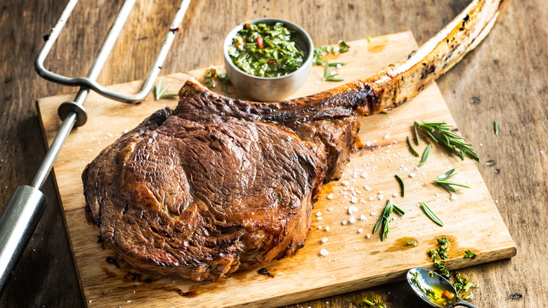 Fogo de Chão tomahawk steak on wood board with rosemary