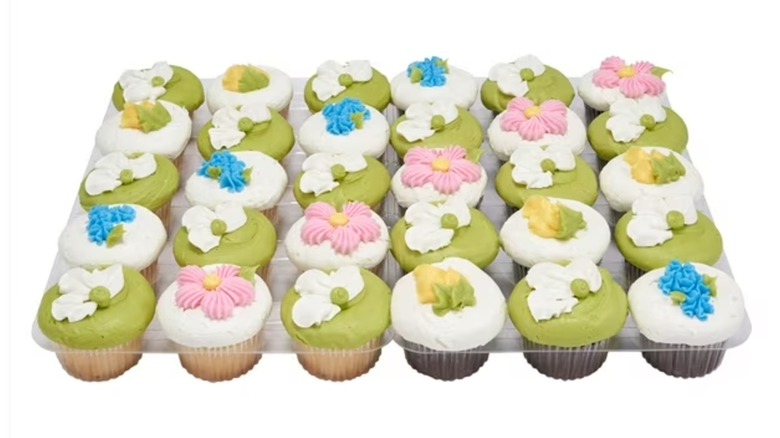 A tray of vanilla and chocolate cupcakes with green or white icing and flowers