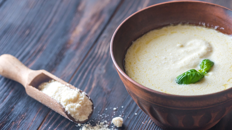 A bowl full of Alfredo sauce on a table with a spoonful of cheese on the side