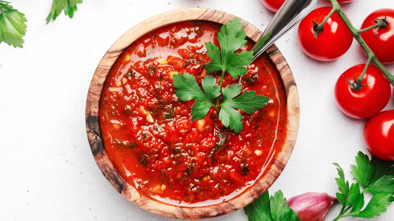 Arrabbiata sauce in a wooden bowl placed on a white table with tomatoes on the side
