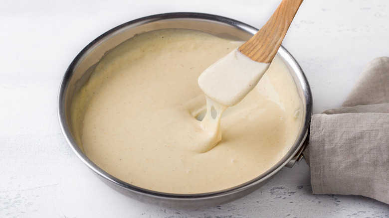 A bowl full of cheese sauce on a white table with a wooden spoon