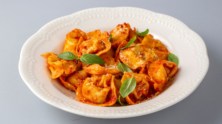A plate full of tortellini tossed in tomato sauce and topped with fresh basil leaves